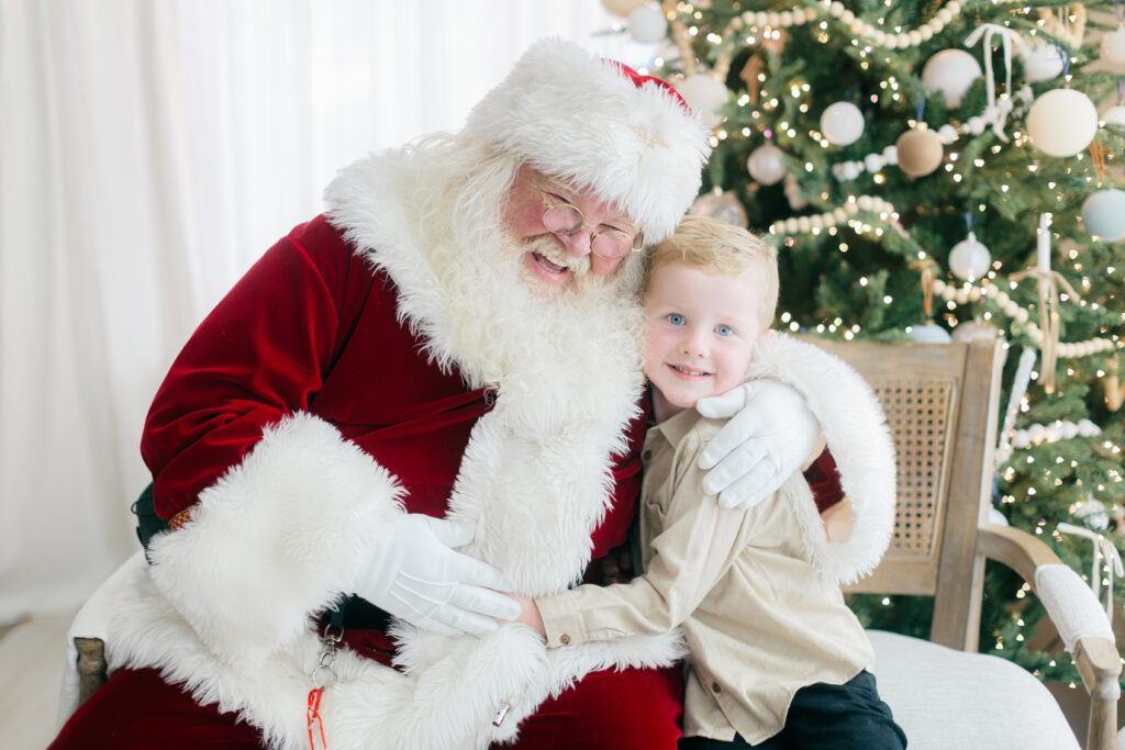 Young boy smiles with Santa during Christmas photo shoot.