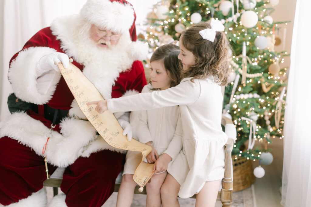 Two sisters look at Santa's nice list during their photo shoot with Santa at our Bentonville studio.