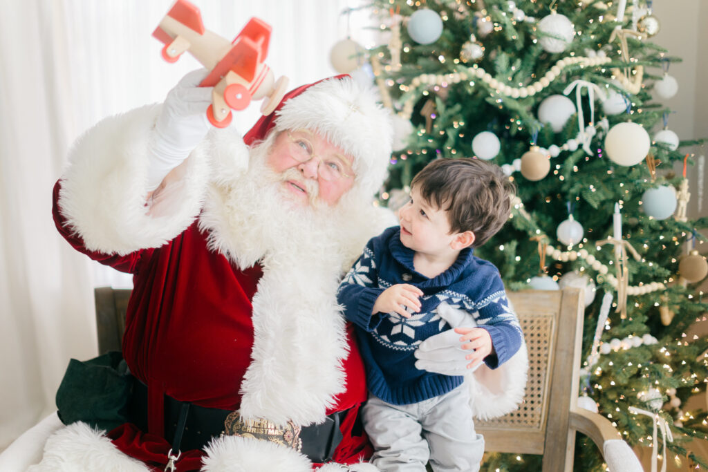 Bentonville Arkansas Santa with toddler boy playing with a red toy airplane.